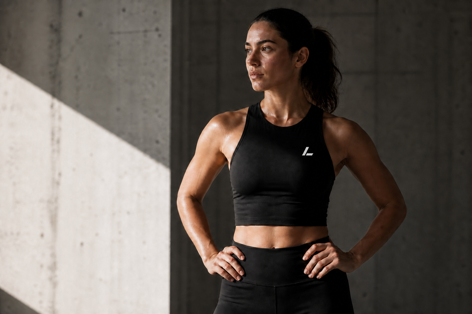 Female LINEAL athlete wearing a black crop top with the angled L logo in a concrete gym